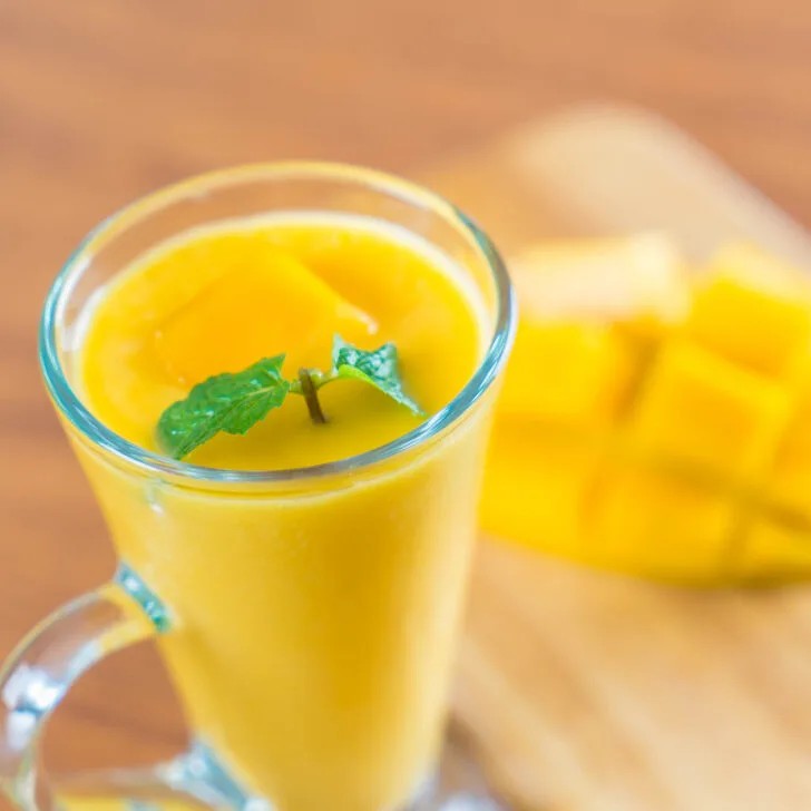 fresh mango and pineapple smoothie in glass with cut up mango