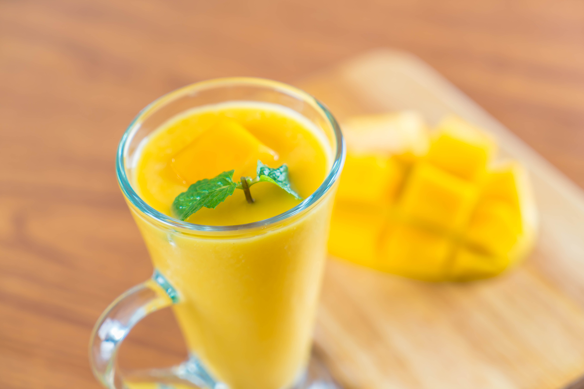 fresh mango and pineapple smoothie in glass with cut up mango 